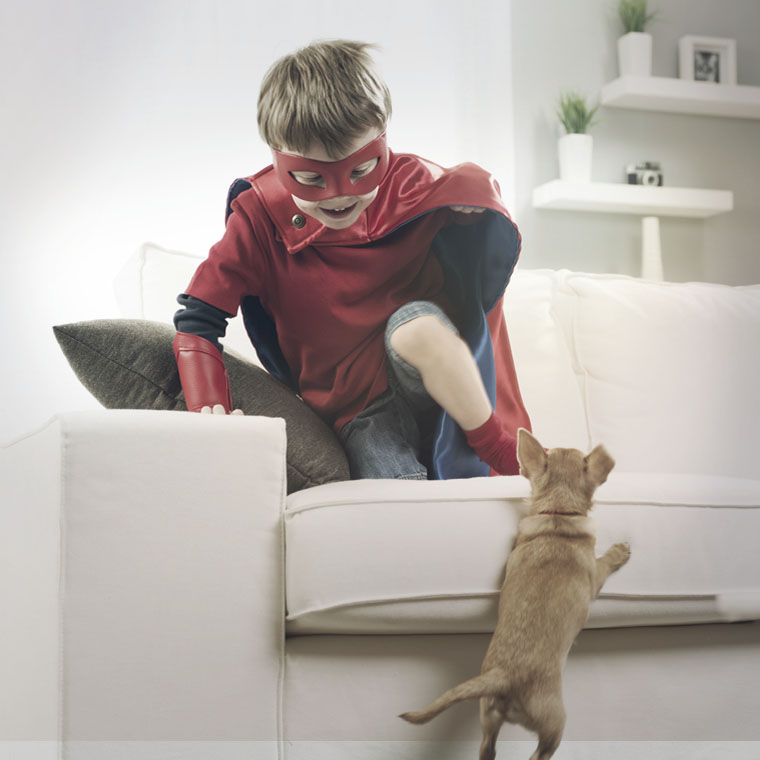 Photo d'un jeune garçon en costume de super héro qui joue avec son chien dans le salon